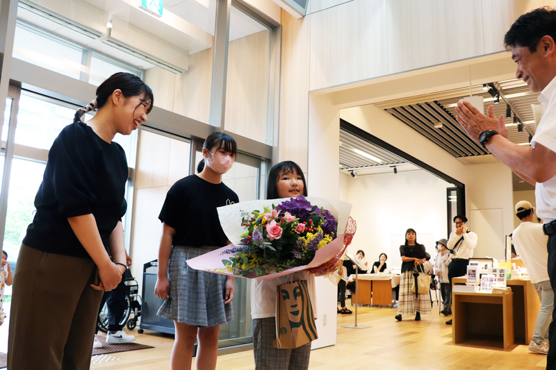 記念すべき100万人目の来館者となった、津﨑さん家族に花束や記念品が贈られている様子の写真