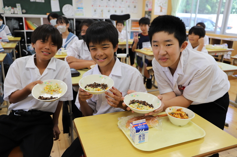 皿に入った給食の石炭ナッツピーを手に取り、笑顔の生徒の写真(1枚目)