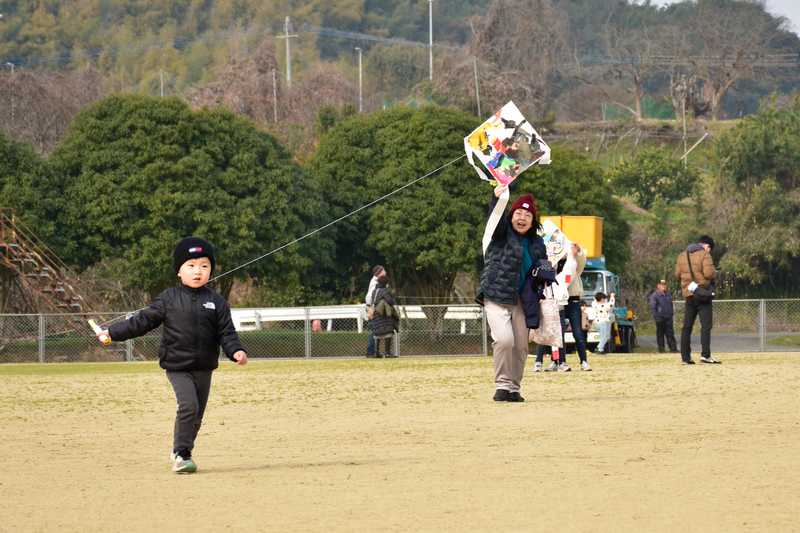 子どもが家族と凧揚げをしている写真