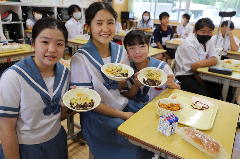 皿に入った給食の石炭ナッツピーを手に取り、笑顔の生徒の写真(2枚目)