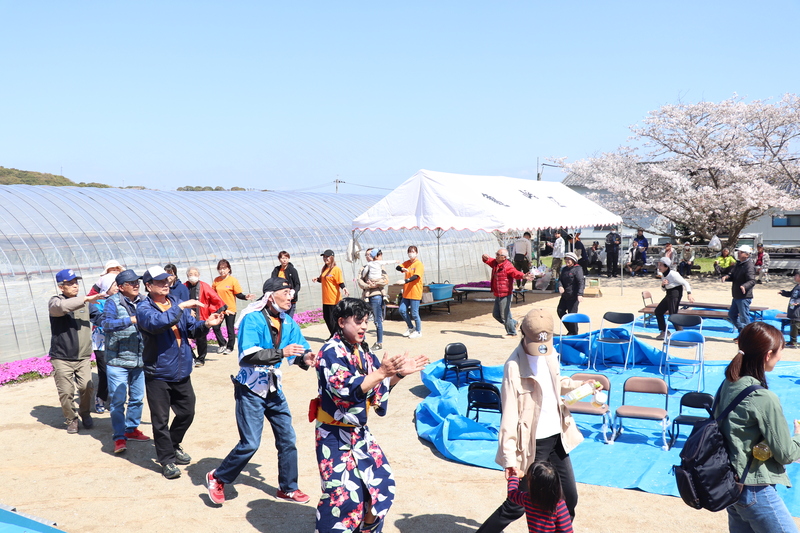 青空の元、不知火まつり歌の音楽に合わせ、輪になって踊る参加者の写真