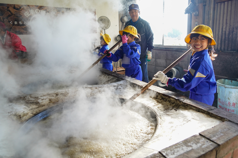 火にかけたサトウキビの汁を混ぜる子供の様子